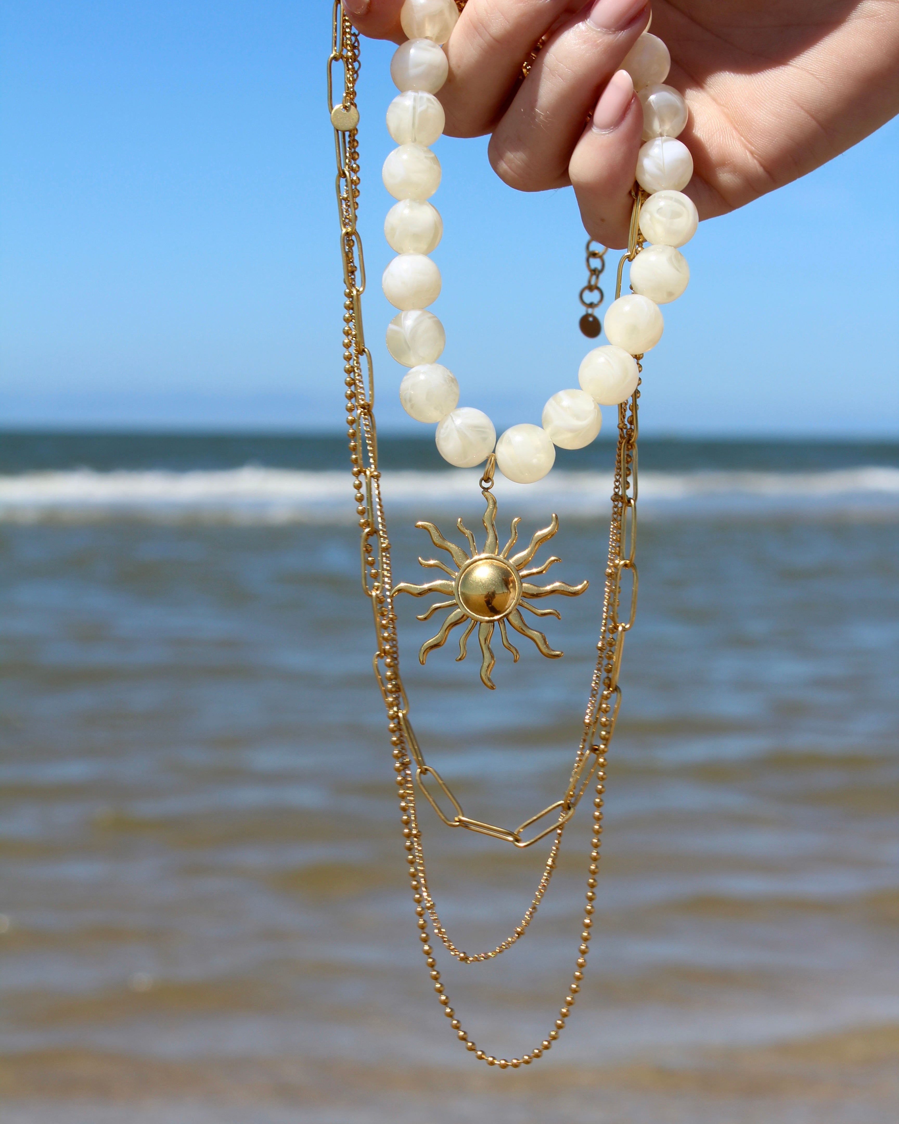 ketting met 3 lagen en een witte kralen ketting met een grote zon bedel