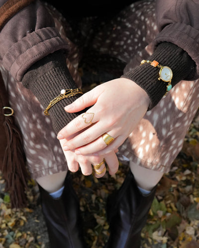 Eloise goldfarbenes 4-lagiges Armband aus Edelstahl mit Gliederketten und weißem Naturstein, getragen über einem schwarzen Pullover