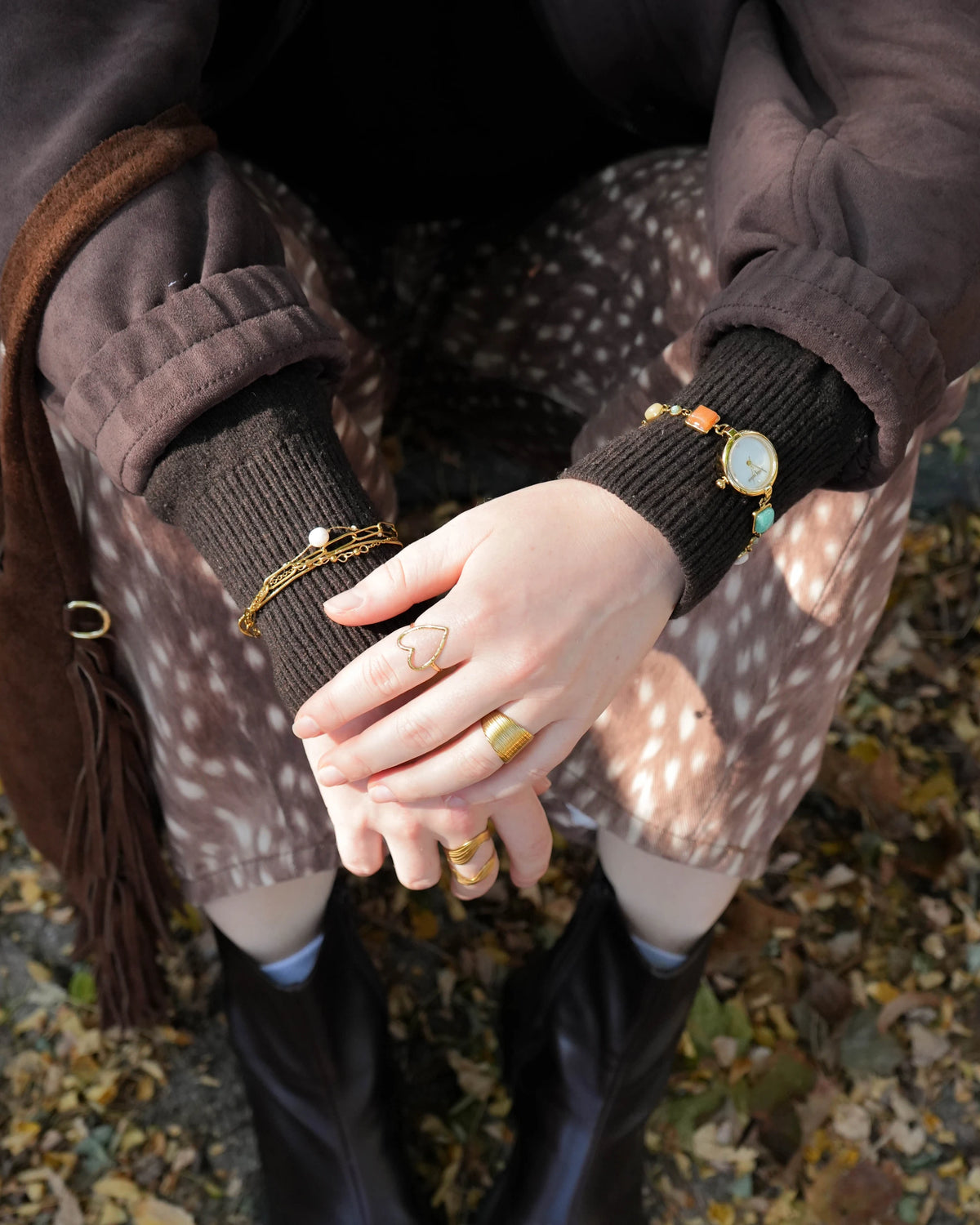 Goldfarbene Dune Uhr mit weißem Perlmutt-Zifferblatt und Gliederarmband mit bunten Steinen, getragen über einem schwarzen Strickpullover